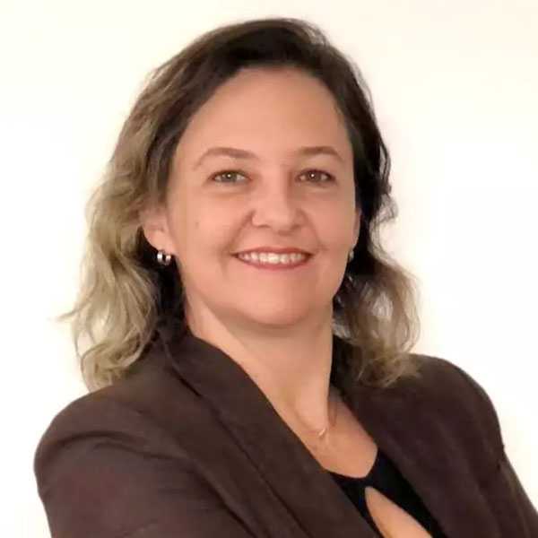 Foto da Dra. Tatiane Calve olhando diretamente para a câmera com um sorriso. Ela veste uma camisa azul e está com o cabelo solto com um fundo branco
